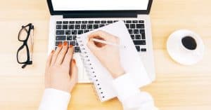 A copy writer in front of a laptop, about to get started with a pen and notebook. | A featured image from "How To Use the Power of Words in Marketing (to Effectively Boost Your Brand)" by LOJO Marketing.