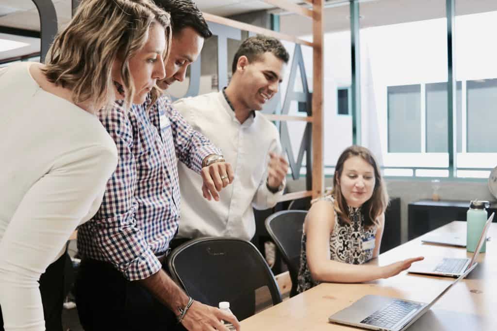 team gathered at a desk and all are looking at a computer